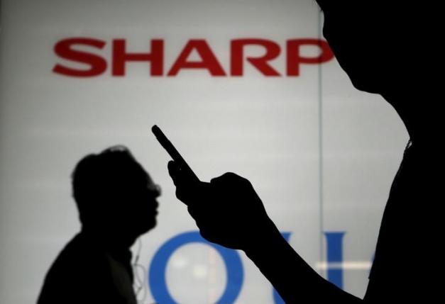 A man using his mobile phone walks past a logo of Sharp Corp outside an electronics shop in Tokyo, Japan, July 31, 2015. REUTERS/Yuya Shino/Files